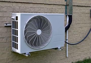 Ductless mini-split AC condenser unit mounted on the side of a home